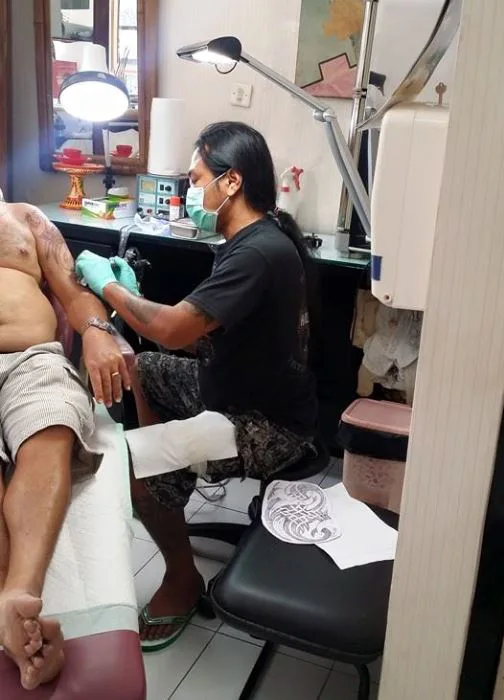 Tattoo artist wearing a mask and gloves tattooing a client's arm in the Demon Tattoo studio
