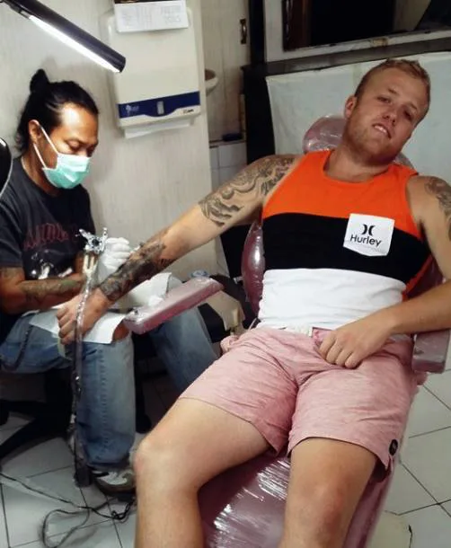 Masked artist tattooing a client's forearm in the studio